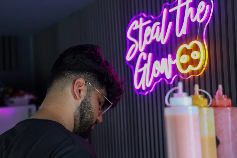 Haysam an der Theke, dahinter der Neonschriftzug Steal the Glow