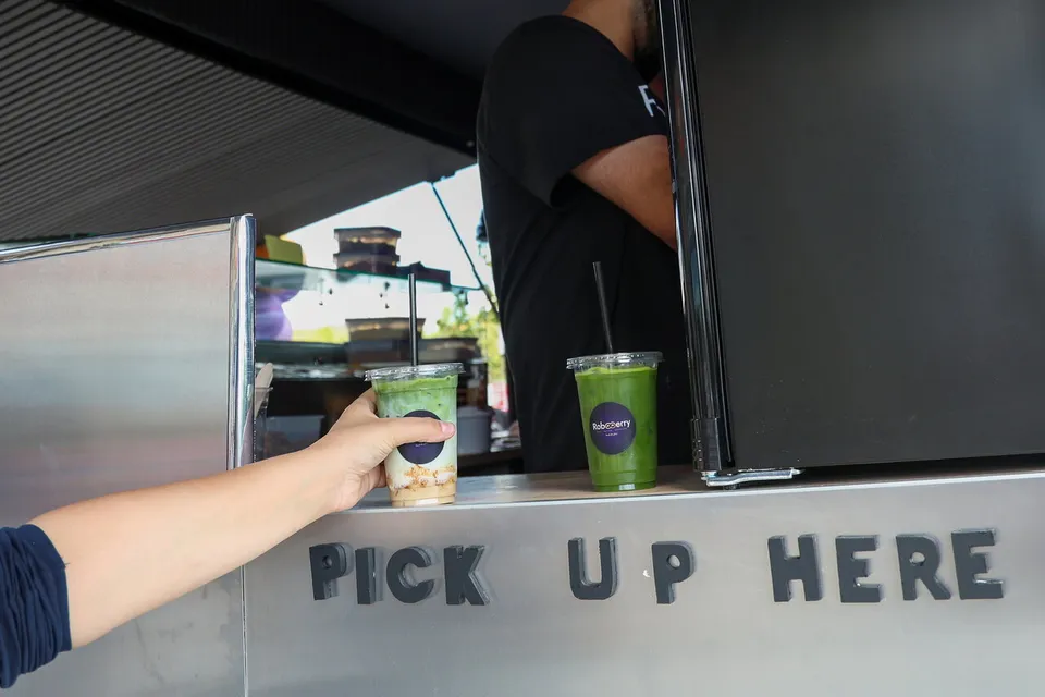 Ein Iced Matcha wird am Fenster „Pick up here“ übergeben